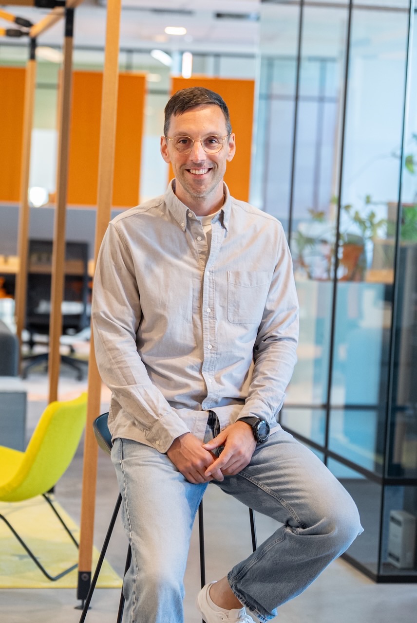 Matthijs van Meurs, AI-trainer, zittend op een kruk in een kantoor met oranje wandpanelen